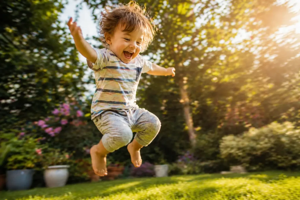 Active toddler jumping in a green garden for physical skill improvement.